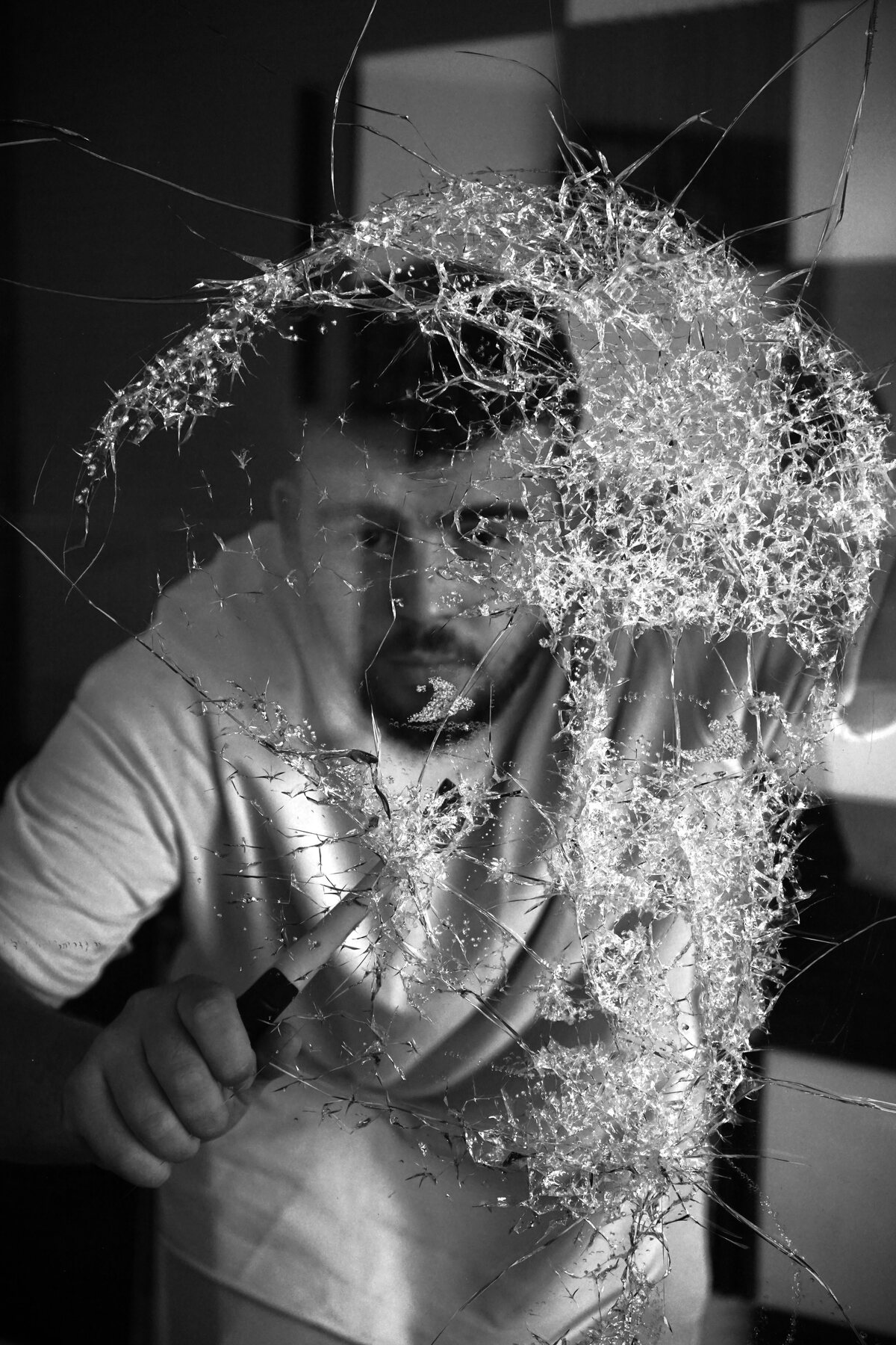 Aron Noka seen through a pane of glass he has fractured, his tool still in hand
