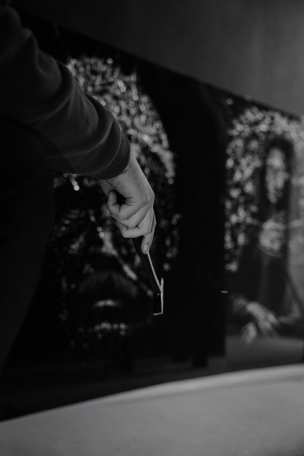 The artist's hand holding a glass-breaking tool before finished fracture portraits